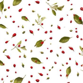 An overhead scattered composition of green leaves and bright red, round berries on a white backdrop photo
