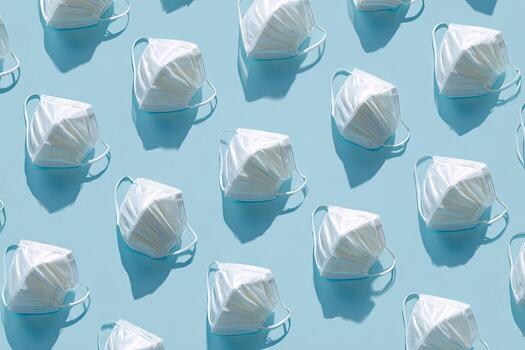 Repeating pattern of white face masks casting shadows on a light blue surface photo