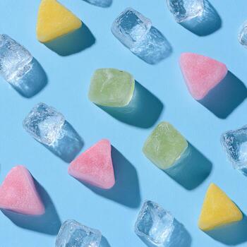 vistoso, geométrico golosinas y hielo cubitos arreglado en un ligero azul superficie fundición oscuridad foto