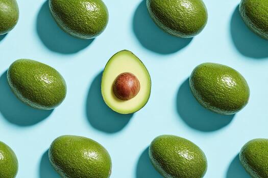 estampado arreglo de todo aguacates con uno rebanado a revelar pozo en contra un ligero azul fondo foto