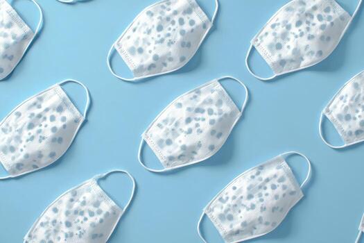 Repeated face masks with gray patterns lie on a light blue surface, slightly angled photo