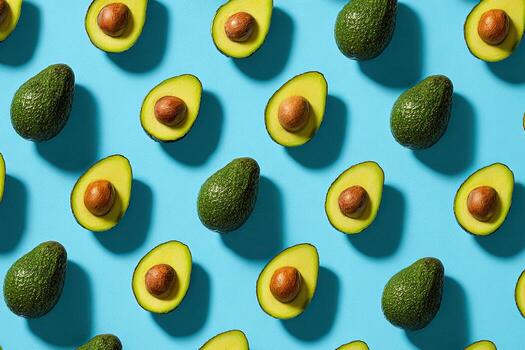 Pattern of sliced and whole green fruit with large pits arranged on bright blue background photo