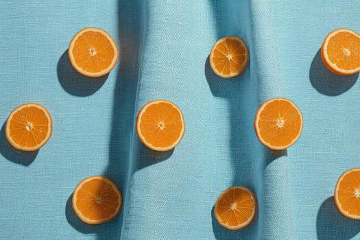 Oranges sliced in half arranged on light blue textured fabric, lit by natural sunlight photo