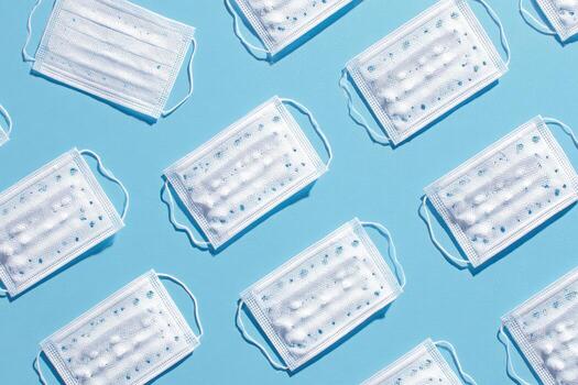 Patterned arrangement of surgical masks against a uniform blue backdrop, overhead shot photo