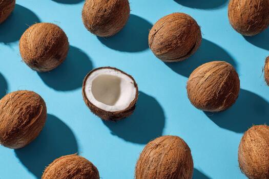 Coconuts, one halved, arranged with shadows on a bright blue backdrop photo