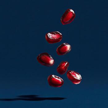 Seven ruby-red pomegranate seeds in freefall against a deep, dark blue gradient photo