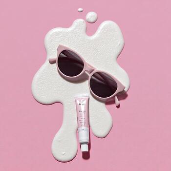 Sunglasses and cream tube rest on a white blob on a pink surface photo