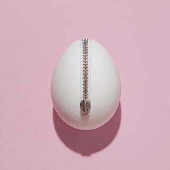 A white, egg-shaped object with a silver zipper down the middle, on pink background photo