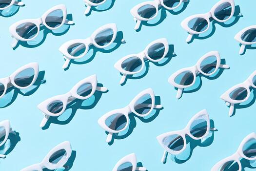 Pattern of retro cat-eye sunglasses on a light blue surface with matching shadows photo