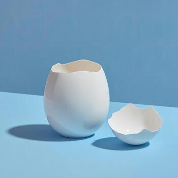 Two white eggshell-shaped ceramic bowls on a light blue surface, with soft shadows photo