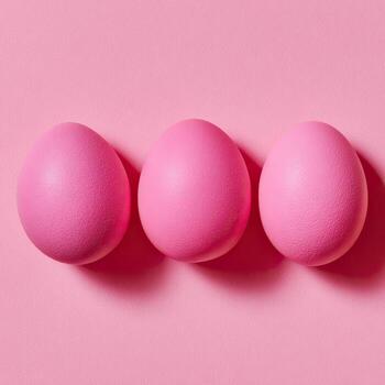 Three pink eggs sit neatly in a row on a similarly colored background photo