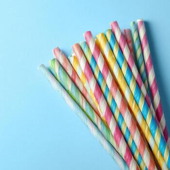 A bundle of colorful striped paper drinking straws arranged on a light blue background photo