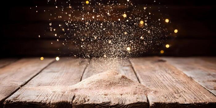 Golden glitter falls onto a rustic wooden surface creating a shimmering pile with bokeh lights in the dark background photo