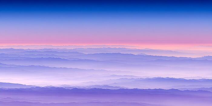 Multiple layers of majestic mountains fade into a purple and blue gradient sky creating a serene and atmospheric landscape at dawn or dusk photo