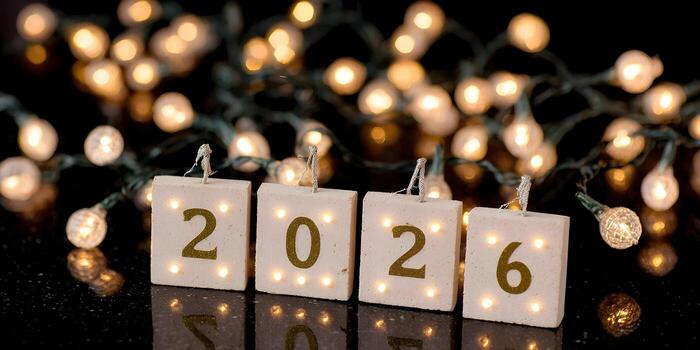 Illuminated blocks spell out the year 2026 on a dark reflective surface with blurred string lights in the background photo