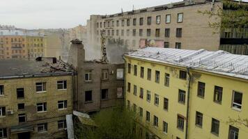 An elevated view captures a yellow excavator in action, methodically tearing down an old gray brick building in a dense urban residential area, creating a cloud of dust and debris video