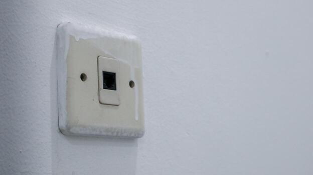 An aged and slightly grimy internet data port, showing wear and tear on a simple, textured white wall, symbolizing dated connectivity photo