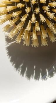 Minimalist top-down view of a round wooden brush with stiff bristles, its stark shadow creating a graphic sunburst effect on a pristine surface photo