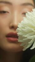 encantador ásia mulher segurando branco flor perto suave jovem beleza face pele brilhando hidratado de natural Cosmético creme sérum anunciar japonês chinês coreano menina fêmea Flor perfume pureza video
