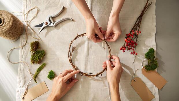 Several hands shape a twig ring on a cloth, preparing a natural Christmas wreath with moss and red berries. photo