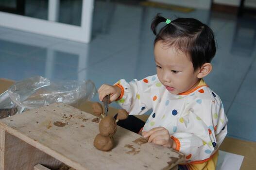 Cute child focused on playing with clay, engaged in the process of creation. The child is seated at a wooden table, molding the clay with focus and care photo