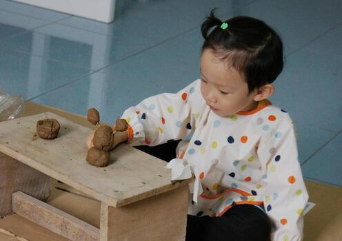 A cute child focused on playing with clay, engaged in the process of creation. The child is seated at a wooden table, molding the clay with focus and care photo