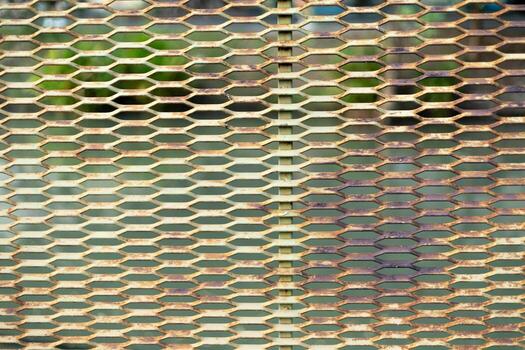 A metallic mesh screen with blurred reflections of greenery behind it. A textured metal fence with light and shadow effects. photo