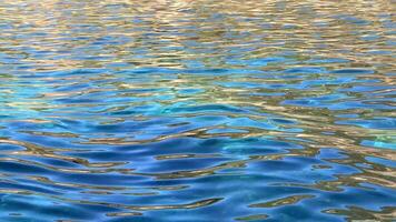 abstrakt se av vibrerande blå och gyllene reflektioner skimrande på de krusigt vatten yta, skapande en komplex mönster av ljus och Färg. video