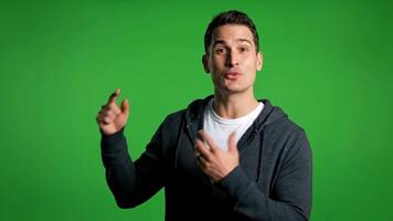 Man in Hoodie Points to Green Screen Background While Smiling video