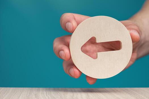 Arrow pointing left on a blue background. Banner with an arrow in a wooden circle in a hand close-up points to the left with copy space. photo