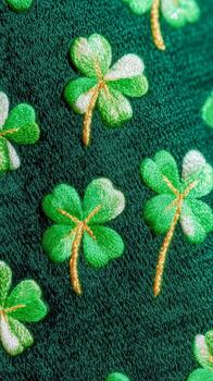 Close-up of a textured green fabric featuring a repeating pattern of embroidered four-leaf clovers. The clovers have light green leaves and yellow stems, creating a festive look. photo