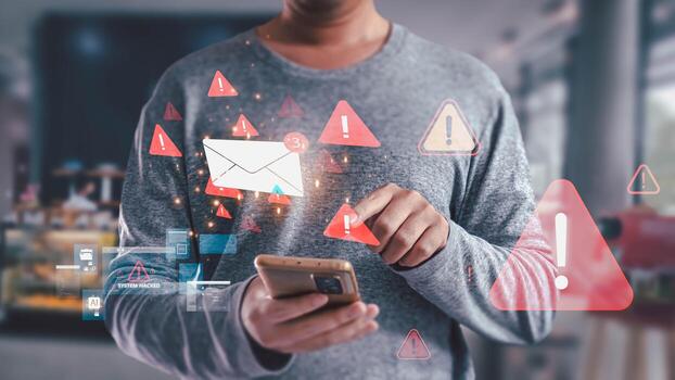 A man holds a smartphone while receiving a spam email notification. The screen displays red warning icons and system hacked alerts, illustrating a cybersecurity phishing scam concept. photo