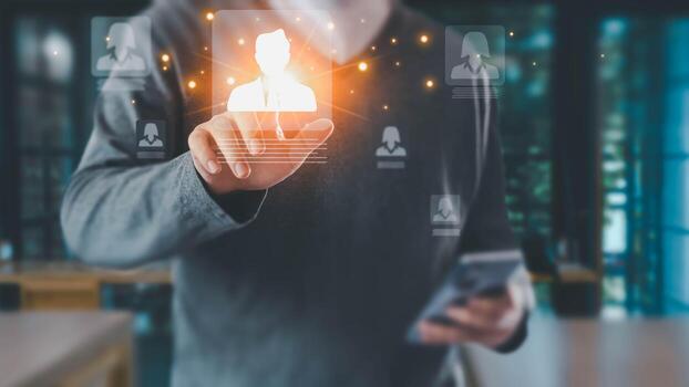 A man in a casual shirt uses a futuristic interface, touching a glowing person icon. This represents concepts like HR, recruitment, and networking in a modern office setting. photo