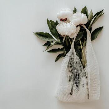 Elegant White Peonies in a Net Bag Against a Light Background During Daylight photo