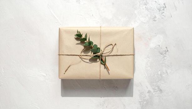 Rustic Kraft Paper Gift Box Tied with Twine and Decorated with Fresh Eucalyptus Branch Overhead Top View on Textured White Background Perfect for Eco Friendly or Natural Themed Presents photo