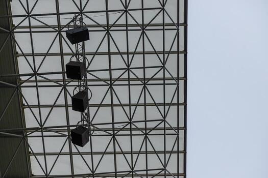 A close-up view of the array of floodlights and public address system speakers attached to the inner framework of the football stadium's roof. photo