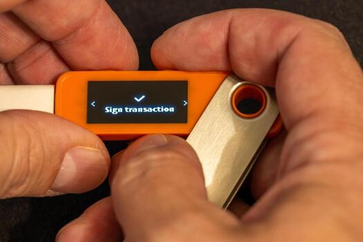 man with light skin signing a transaction using orange hardware wallet with small screen photo