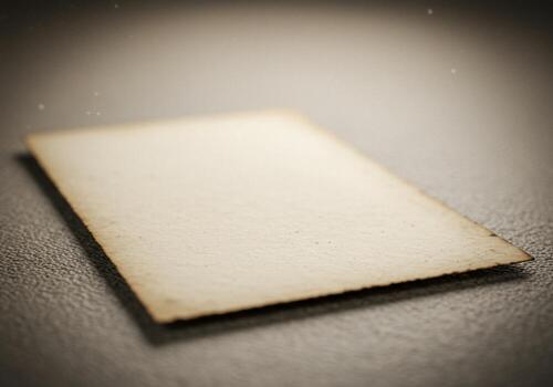 Aged paper card with darkened edges on textured surface in soft, diffused lighting photo