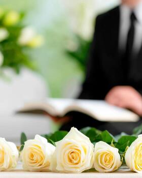 Close-up of white roses on a table at a funeral with a man reading scripture in the background photo
