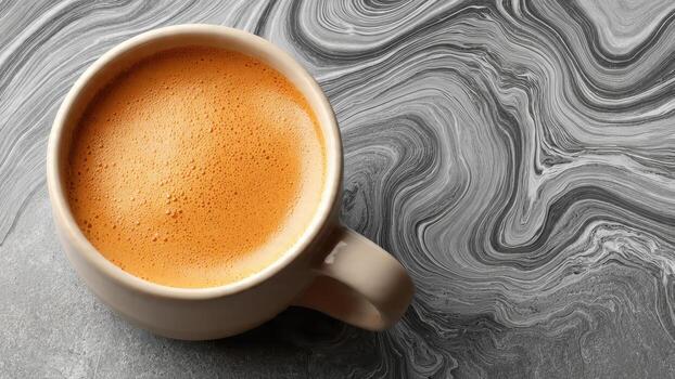 A cup of coffee with frothy foam rests on a gray textured surface with swirling gray patterns photo