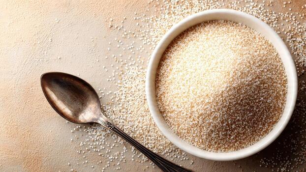 A white bowl overflows with amaranth grain next to a vintage metal spoon on a textured surface photo