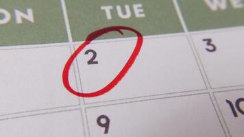 il 2 ° Data su un' calendario è cerchiato con un' rosso marcatore nel un' avvicinamento macro tiro su un' bianca pagina, simboleggiante un importante giorno o promemoria. video