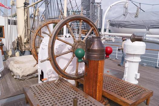 Historic ship wheel and navigation lights aboard a tall ship in a city harbor during the day photo