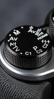 Close up view of a black camera mode dial with various settings like manual aperture priority and program displayed photo
