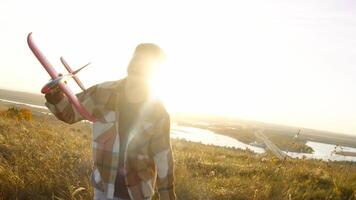 Medium close-up shows boy joyfully running toward camera, lifting toy airplane as evening sunlight streams through autumn field and tree branches in background. video