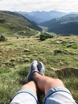 A guy sits on the edge of a mountain overlooking a winding road A man is sitting on the grass in the mountains photo