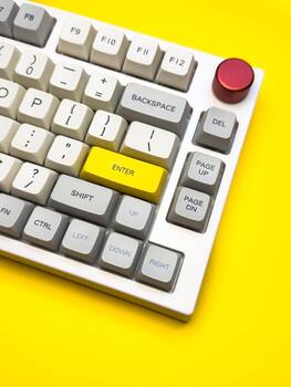 Vertical White mechanical keyboard with bright Enter key on bright yellow background, minimalism, keyboard buttons. A keyboard with a yellow key on the bottom left photo