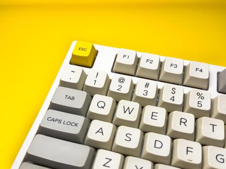 Close up mechanical keyboard with bright Esc key on bright yellow background, minimalism, keyboard buttons. A keyboard with a yellow key on the bottom left photo