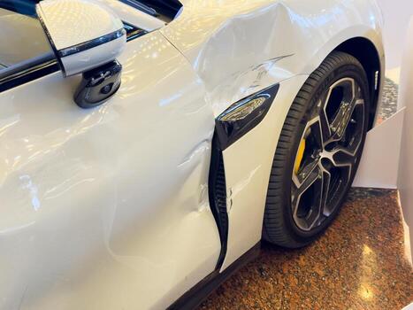 Close up of a deep scratch and dent on a white car door and a wing, showing damaged paint, metal tear, and surface abrasions. photo
