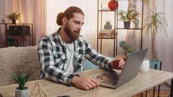 homem concentrados às casa mesa, digitando em computador portátil até tropeçando sobre uma grande falha erro vírus este faíscas imediato aborrecimento. cara tapas testa, silenciosamente resmungando às inesperado técnico questão falhou video